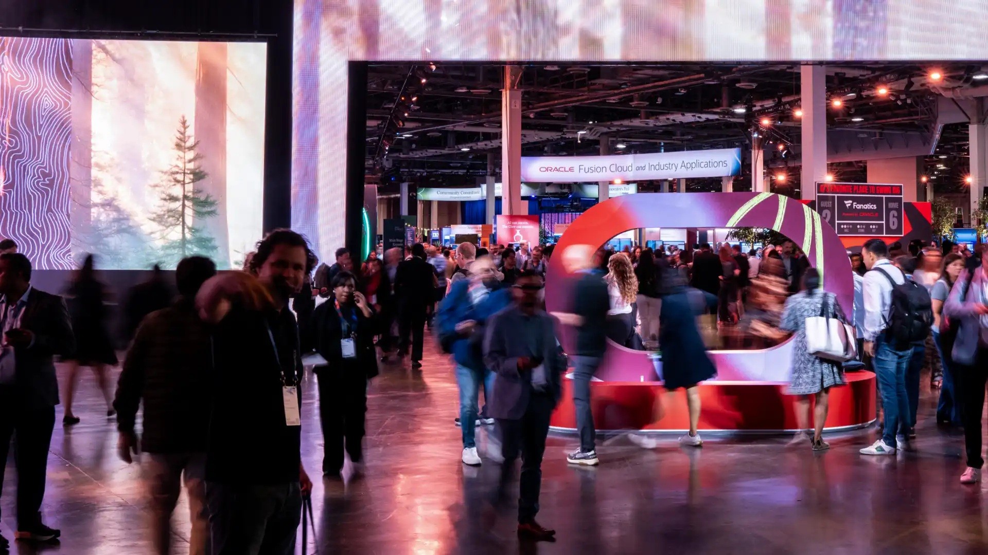 Attendees walk through the exhibition area, with an Oracle Fusion Cloud and Industry Applications sign in the background.
