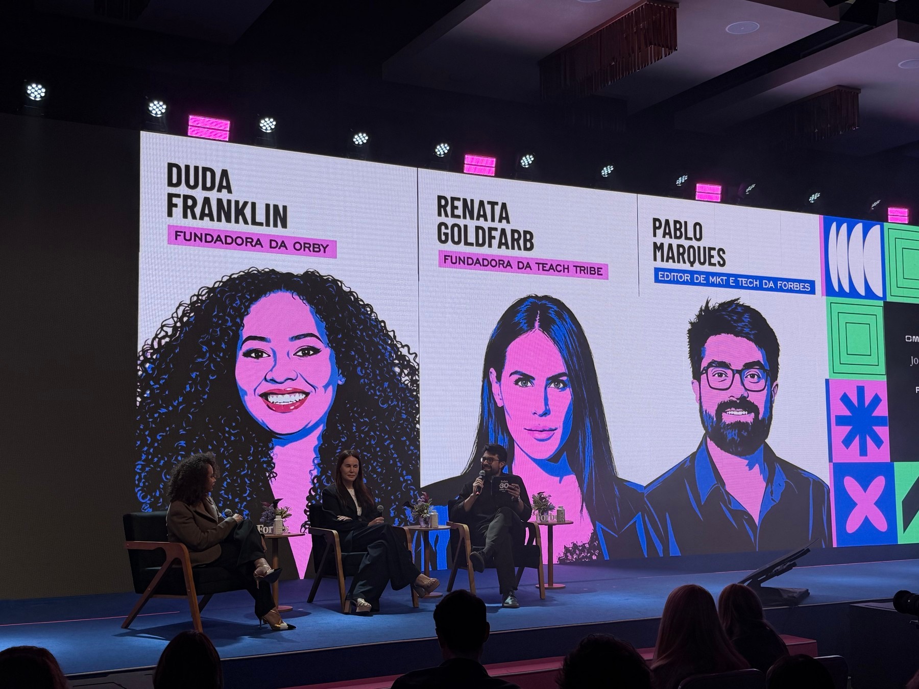 The AI First panel on stage, with the names Duda Franklin, Renata Goldfarb and Pablo Marques on the screen.