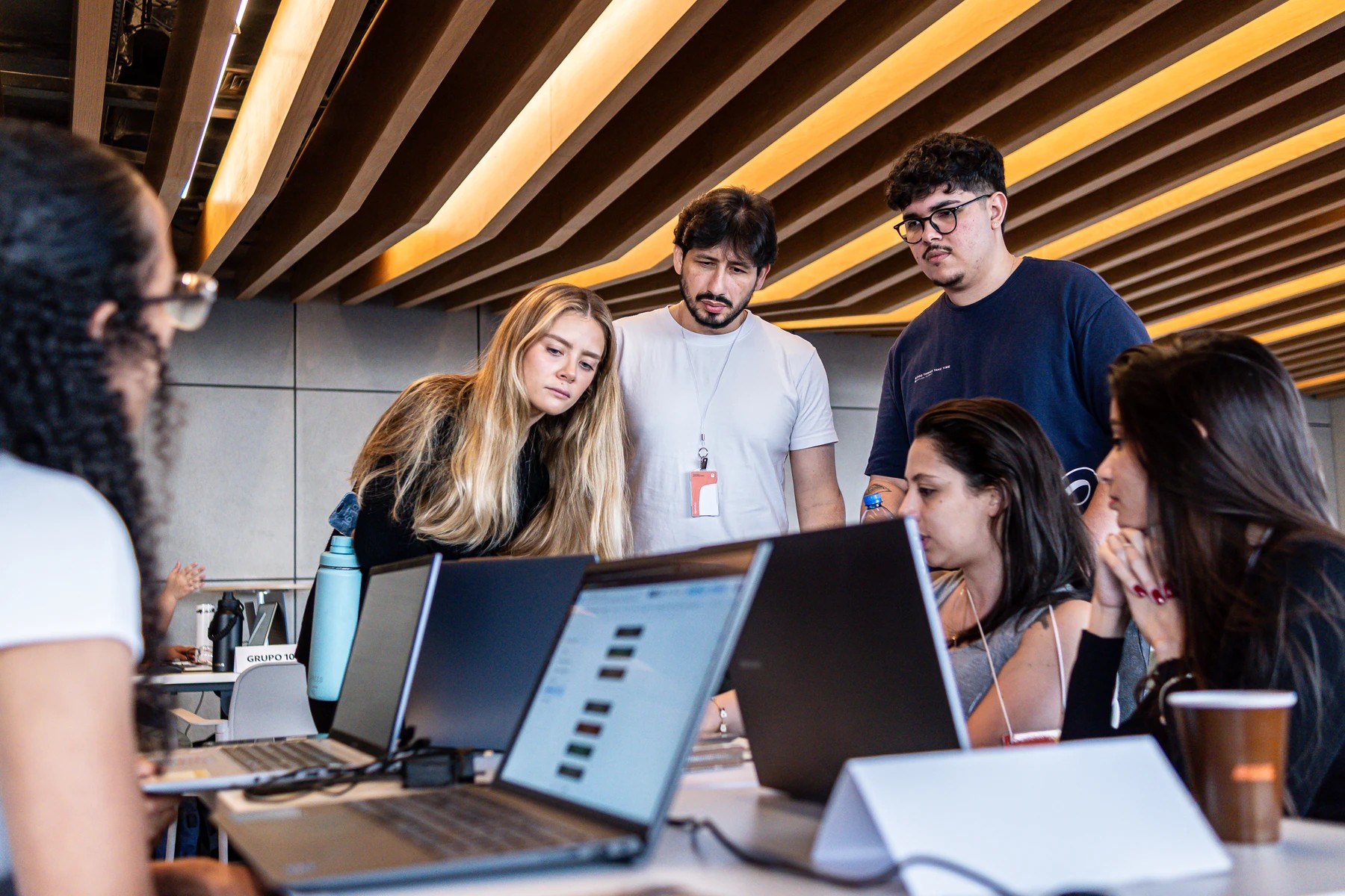 Participantes e mentores conversam em torno de computadores durante o hackathon do Itaú