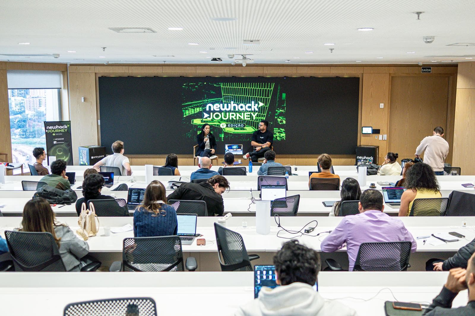 Sala do NewHack Journey dentro da ADAPTA, no Berrini One, com founders assistindo a um painel