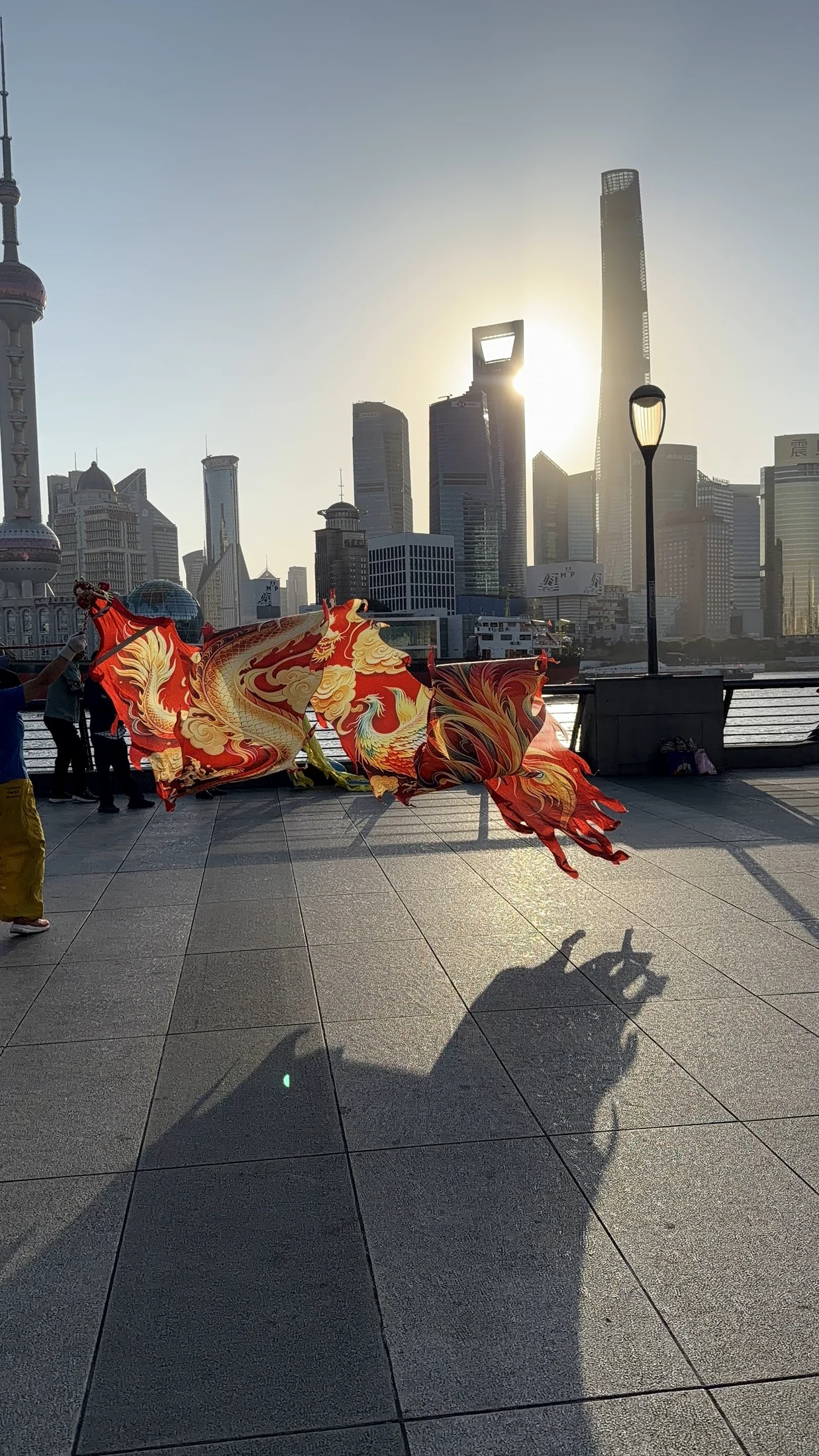 Tecido vermelho e dourado em movimento, com o skyline de Xangai ao fundo.