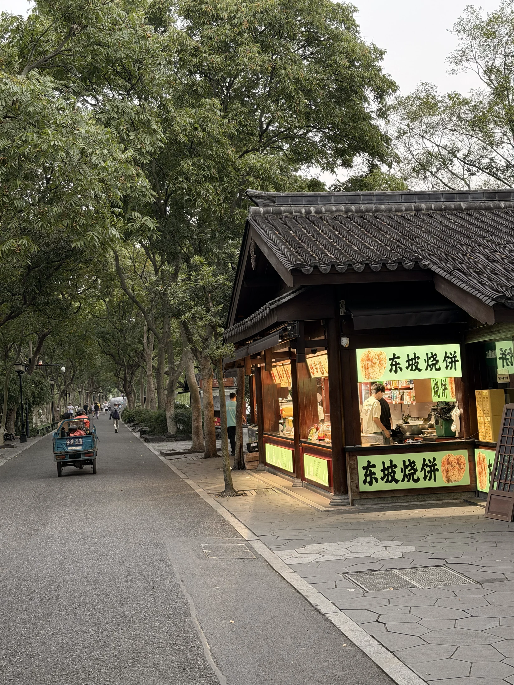 Rua arborizada com comércio e movimento no início da manhã em Hangzhou.